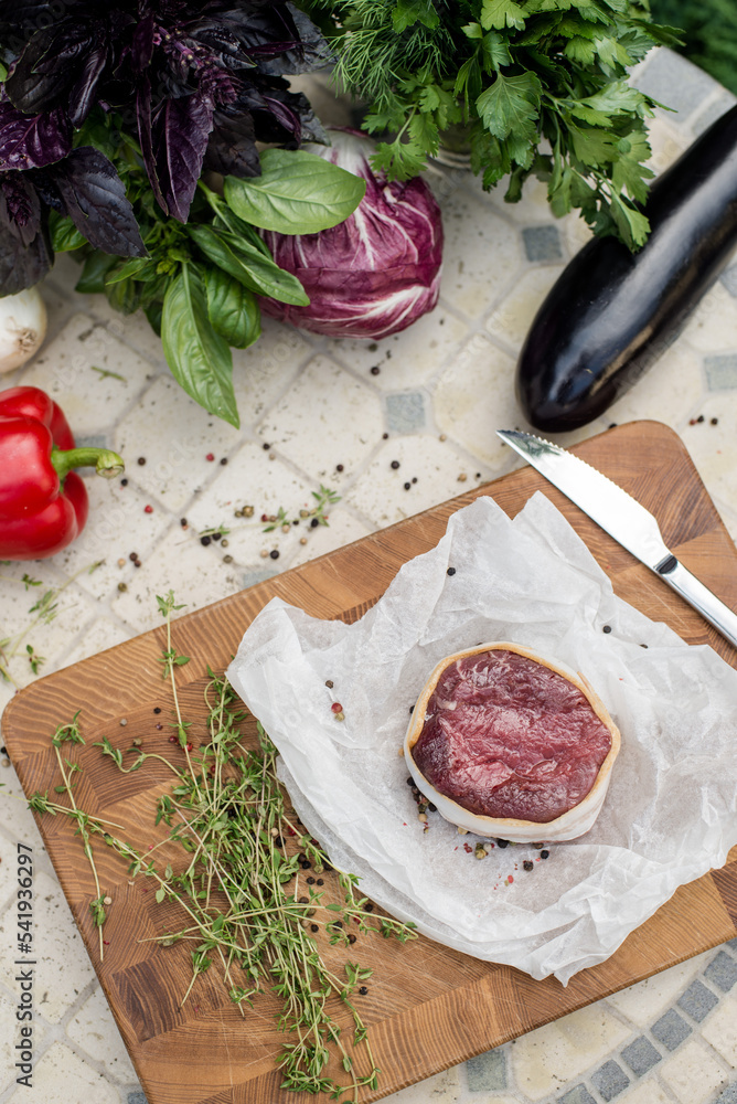 Raw beef steak before cooking. Fresh steak on wooden board among greens and vegetables. Summer grill