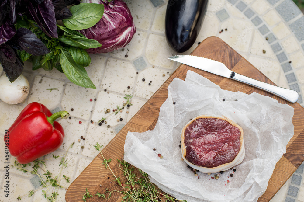 Raw beef steak before cooking. Fresh steak on wooden board among greens and vegetables. Summer grill. Cooking at home