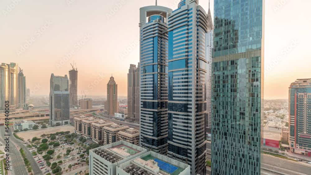 Aerial panorama of Dubai International Financial District with many skyscrapers timelapse during all day with shadows moving fast. Traffic on a road near parking lot with rooftop tennis court. Dubai Aerial panorama of Dubai International Financial District with many skyscrapers timelapse during all day with shadows moving fast. Traffic on a road near parking lot with rooftop tennis court. Dubai