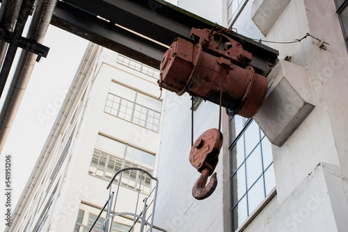 old factory exterior with large metal beam and electric rail cable hoist. Industrial background. White buildings. Heavy machinery and equipment. 