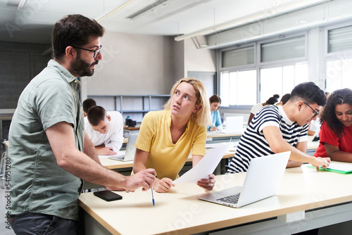 Young male teacher helping female student in class. The tutor helping his students by explaining the lesson and solving doubts. High quality photo