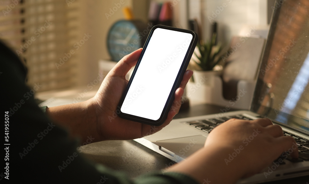 Close up view of woman hand holding mobile phone and using laptop computer. Close up view of woman hand holding mobile phone and using laptop computer.