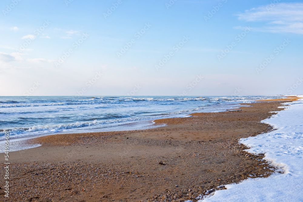 Winter seascape. Blue sea and sandy shore with fallen snow