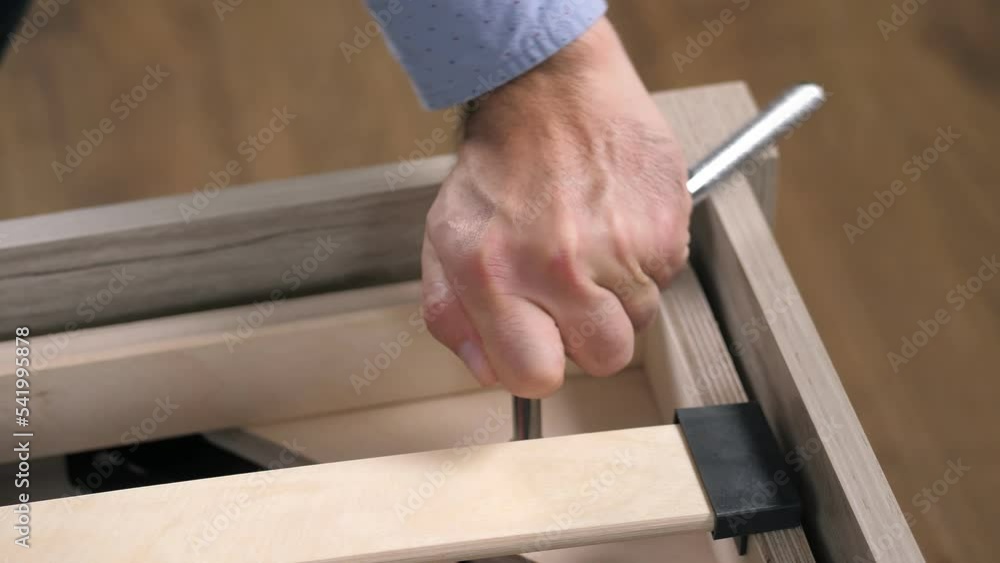 Close-up of a man's hands assembling a wooden bed using a hexagon to insert screws into the bed frame.Collection of wooden furniture.Husband for an hour.Self-assembly using a guide. House design Close-up of a man's hands assembling a wooden bed using a hexagon to insert screws into the bed frame.Collection of wooden furniture.Husband for an hour.Self-assembly using a guide. House design