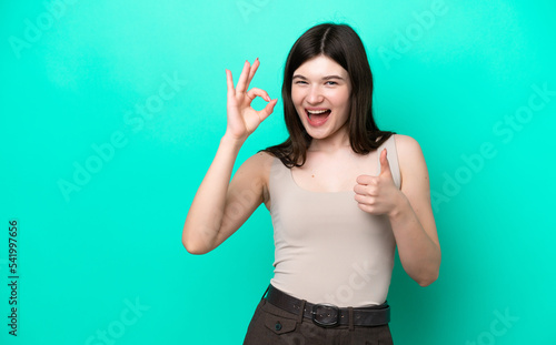 Young Russian woman isolated on green background showing ok sign and thumb up gesture