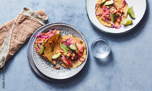 Salmon papaya tacos on two plates on blue surface