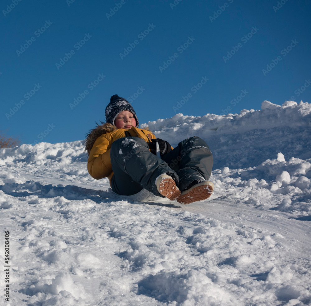 happy boy sliding down snow hill on sled outdoors in winter, sle