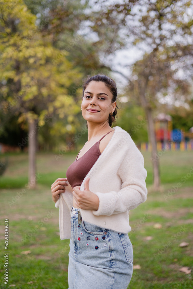 Smiling girl in the park wearing a short maroon blouse, a white jacket and a denim skirt, looking at the camera. Smiling girl in the park wearing a short maroon blouse, a white jacket and a denim skirt, looking at the camera.