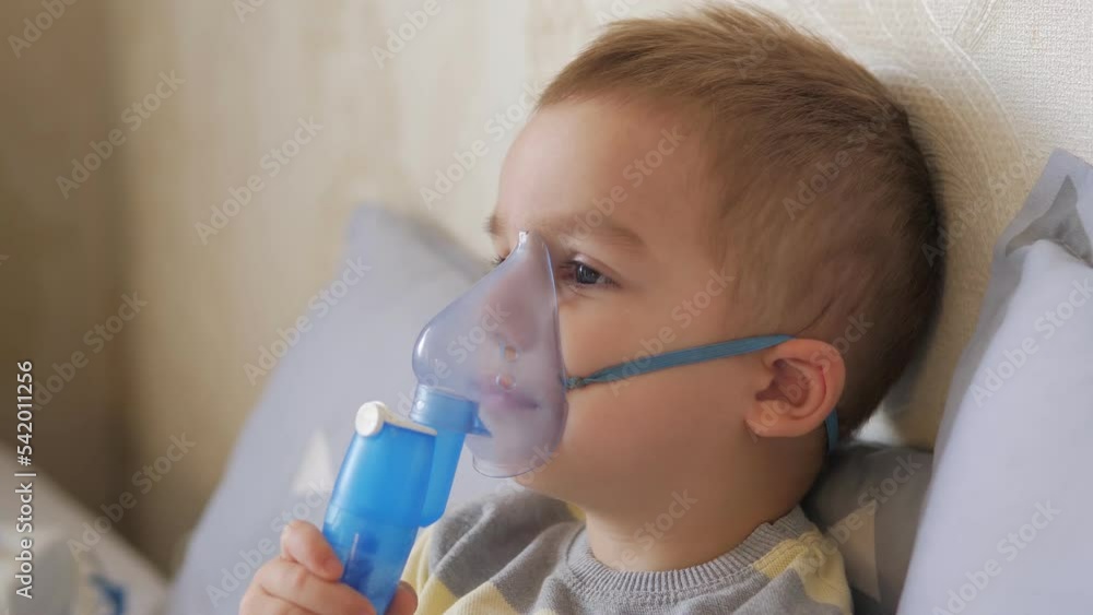 Little 2 years old boy does therapeutic inhalation using a nebulizer.Child takes a breath through inhaler mask at home.Kid treats inflammation of airways via nebulizer for preventing asthma and cough. Little 2 years old boy does therapeutic inhalation using a nebulizer.Child takes a breath through inhaler mask at home.Kid treats inflammation of airways via nebulizer for preventing asthma and cough.