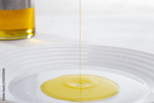 Extra virgin olive oil jet falling on white plate forming creative figure