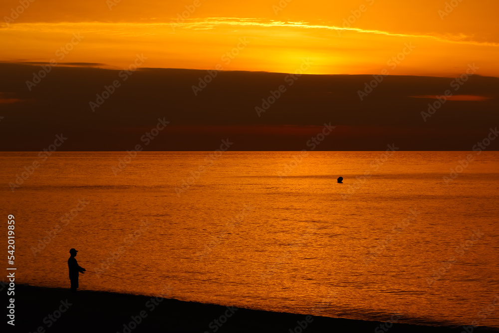 Espectacular amanecer con cielo naranja y silueta de un pescador