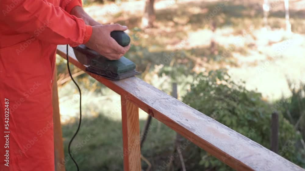 man in a red boilersuit is sanding wood plank with old varnish coating with a grinder man in a red boilersuit is sanding wood plank with old varnish coating with a grinder