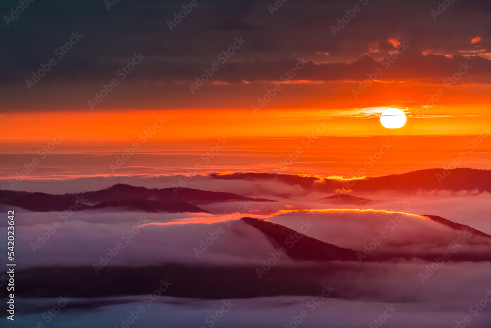 Clouds inversion at sunrise morning dawn in Wintergreen Resort, Virginia ski resort town with colorful red sun rising above horizon with sunlight fog sky in Blue ridge mountains
