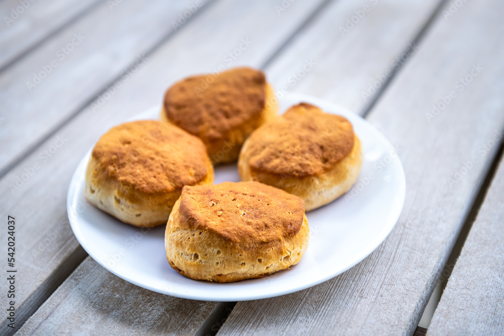 Macro closeup on four cooked homemade buttermilk breakfast biscuits on white plate at kitchen wooden table Macro closeup on four cooked homemade buttermilk breakfast biscuits on white plate at kitchen wooden table