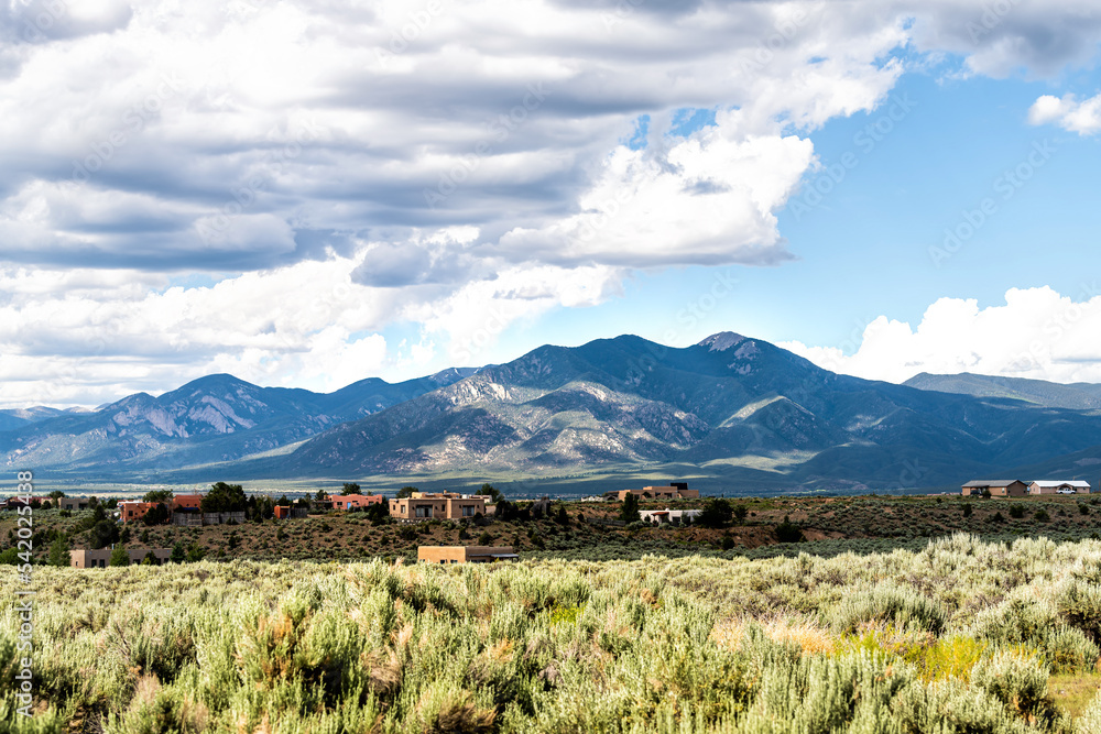Fototapeta premium View grass green desert sage brush plants in Ranchos de Taos valley, New Mexico with Sangre de Cristo mountains landscape in summer