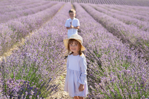 Cute boy with a bouquet in his hands walks through a field of lavender to a girl in a dress and hat