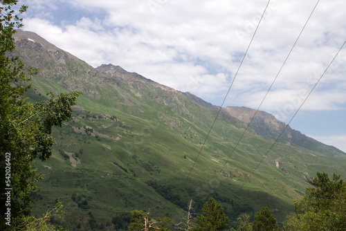 Beautiful landscape - green mountain slopes with trees and white clouds on a blue sky on a sunny summer day in the Terskol valley in the Elbrus region and copy space