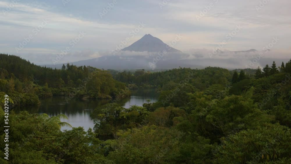 Mount Taranaki at sunset, with a forest and a river in the foreground, in New Zealand Mount Taranaki at sunset, with a forest and a river in the foreground, in New Zealand