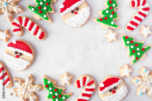 Cute Christmas cookie frame. Top down view on a white marble background with copy space. Holiday baking concept. Santa Claus, tree, snowflakes, candy canes, stars.