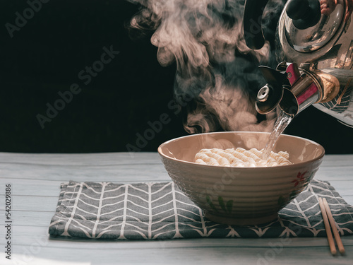 Steam and smoke Instant noodles in bowl on wooden table and nature light and black background, selective focus. It is a convenient and inexpensive food, but eating often is not good for health.