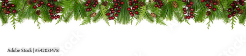 Winter top border with evergreen branches, dark red berries and pine cones. Overhead view isolated on a white banner background.