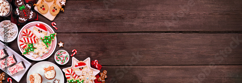 Cute Christmas sweets and cookie corner border. Above view on a rustic dark wood banner background with copy space. Fun holiday baking concept.