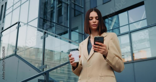 Bisnesswoman browsing phone, holding coffee and standing near a business center photo