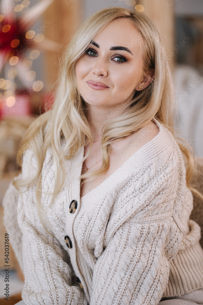 Portrait of blond hair woman in hoodie open present on Chrisrmas time. Elegant woman stand by big Christmas tree in front of window Portrait of blond hair woman in hoodie open present on Chrisrmas time. Elegant woman stand by big Christmas tree in front of window
