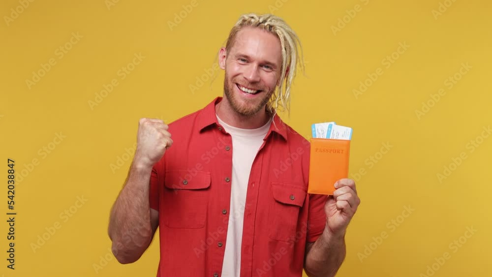 Traveler man with dreadlocks wear red shirt hold passport boarding tickets isolated on plain yellow color background studio. Tourist travel abroad in free spare time getaway. Air flight trip concept Traveler man with dreadlocks wear red shirt hold passport boarding tickets isolated on plain yellow color background studio. Tourist travel abroad in free spare time getaway. Air flight trip concept