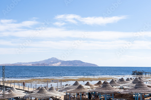 Fototapeta Naklejka Na Ścianę i Meble -  Mediterranean coast with sunbeds and straw sun umbrellas on the sandy beach