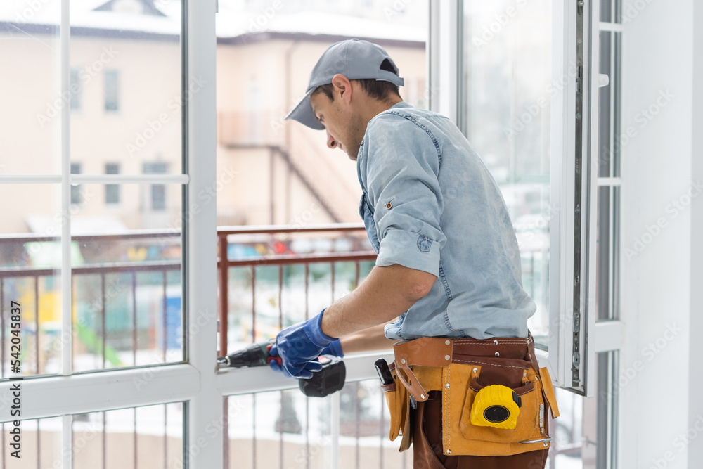 Construction worker installing window in house. Handyman fixing the window with screwdriver Construction worker installing window in house. Handyman fixing the window with screwdriver