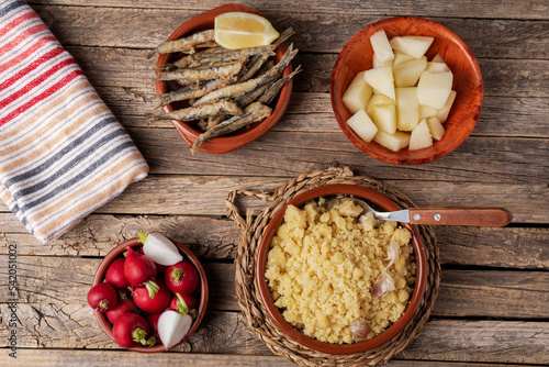 Rustic dish with migas, traditional Spanish food, accompanied with radishes, fish and melon on an old wooden table. Top view.