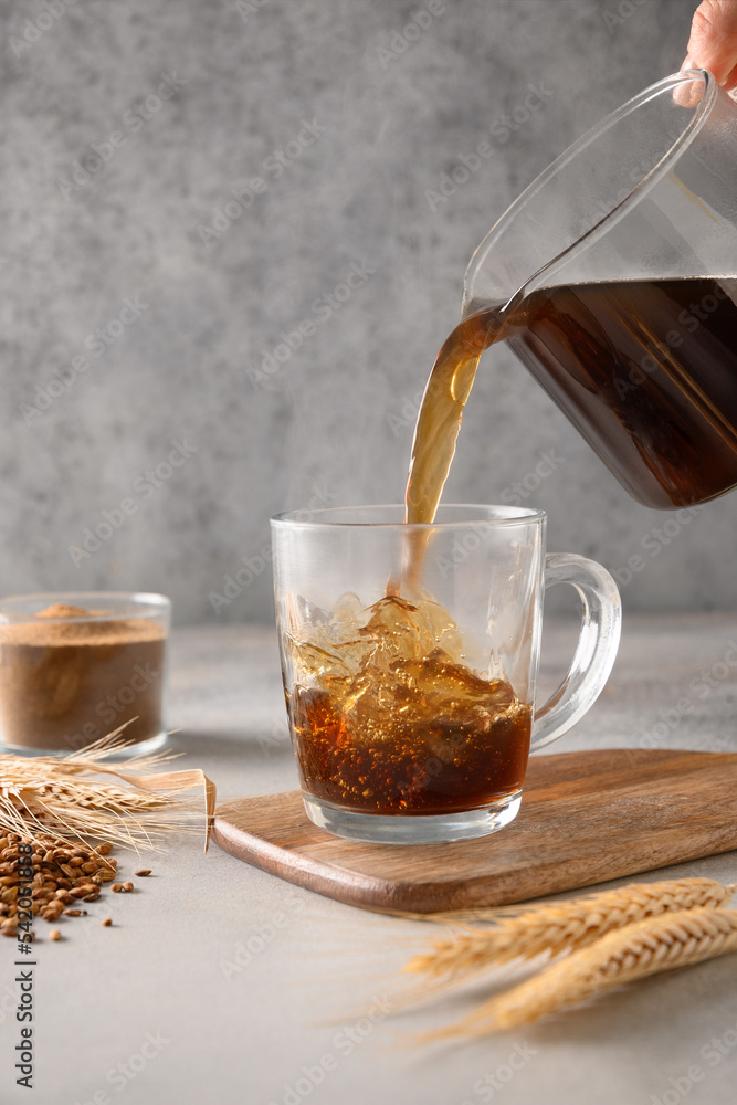 Fototapeta premium Pouring barley coffee in glass cup on gray background. Cooking healthy caffeine free alternative coffee. Close up. Vertical format.