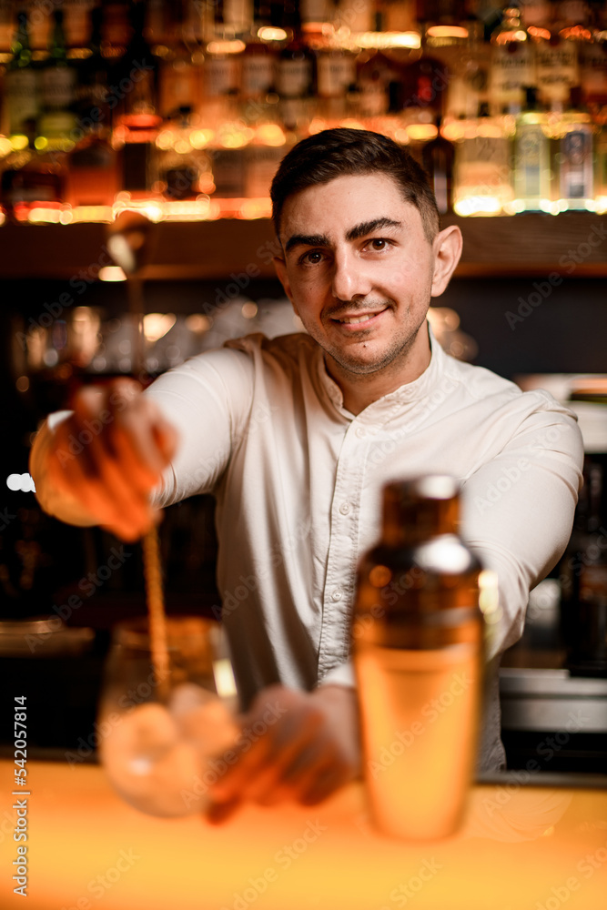 selective focus on face of male bartender mixing cocktail in glass with spoon.