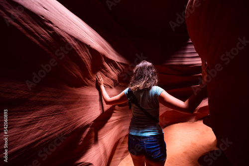 Young woman back inside Upper Antelope slot canyon, Arizona standing leaning touching sandstone rock formations between walls