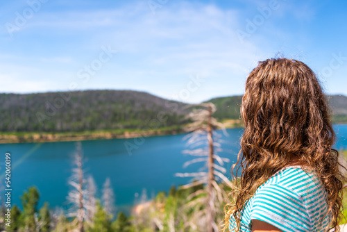 Young woman back looking at view of Navajo lake Kane county water reservoire in Utah with pine spruce trees forest in summer photo