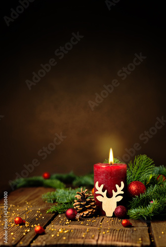 Kerze zum 1. Advent und Weihnachten. Dekoration mit roter Adventskerze, Tannenzweigen, Zapfen, Kugeln und Rentier auf Holz. Hochformat mit Textraum