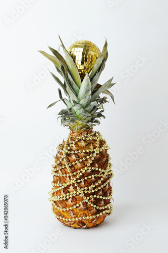 Pineapple decorated like a Christmas tree. Gold beads garland. Golden shining reflective disco ball. White background
