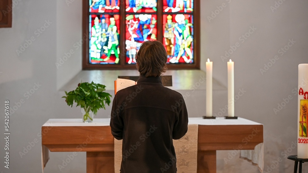 Back view of a young man praying at the altar in a church
