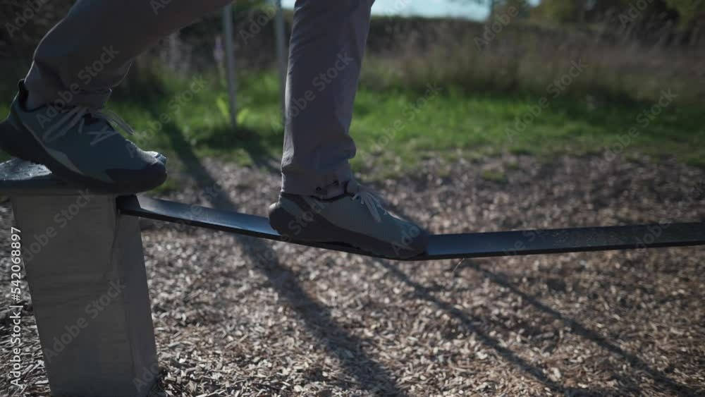 Beginner man in shoes learns to walk and keep balance on rubber slackline in park in Germany. Man balances on stretched rope at city gym in Munich. Slacklining. Slackline band. Balancing rubber rope. Beginner man in shoes learns to walk and keep balance on rubber slackline in park in Germany. Man balances on stretched rope at city gym in Munich. Slacklining. Slackline band. Balancing rubber rope.