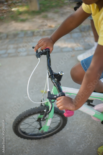 Close-up of bicycle handlebar and African American kid hands on it. Little boy riding small bike in street in summer. Leisure, active rest and children health concept