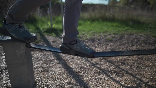 Beginner man in shoes learns to walk and keep balance on rubber slackline in park in Germany. Man balances on stretched rope at city gym in Munich. Slacklining. Slackline band. Balancing rubber rope. 