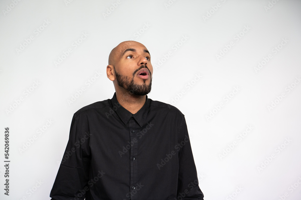 Portrait of shocked young man with open mouth. Surprised multiethnic male model with bald head and beard in black shirt looking away at something unusual. Shock, advertisement concept Portrait of shocked young man with open mouth. Surprised multiethnic male model with bald head and beard in black shirt looking away at something unusual. Shock, advertisement concept