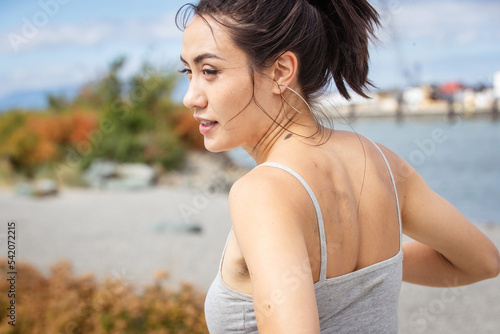 Pretty Asian woman from behind. She is wearing a gray tank top and has a muscular back.