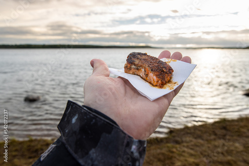 Fresh grilled salmon meat with cajun spice held in hand by fisherman near river where the fish was recently caught for a fresh seafood meal. photo