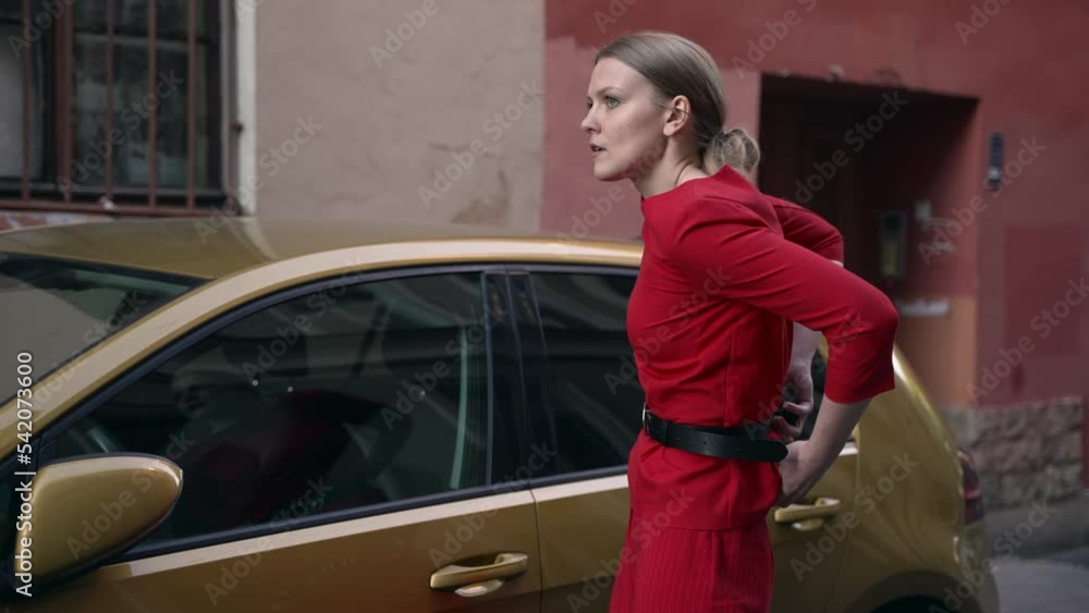 4k Young woman holds gun and stands by car on city street spbd. Beautiful female is holding black weapon and hiding it behind her clothes, standing by transport in modern town. One millennial hitman 4k Young woman holds gun and stands by car on city street spbd. Beautiful female is holding black weapon and hiding it behind her clothes, standing by transport in modern town. One millennial hitman