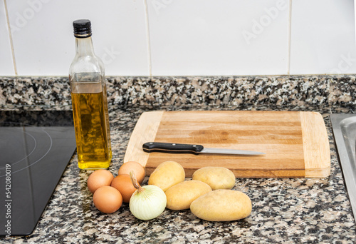 Potatoes, oil and onion in a kitchen with a wooden board on top of a marble table .Concept of preparing an traditional spanish omelette