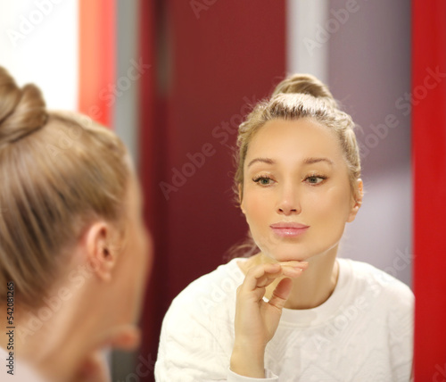 woman looking in the mirror in the bathroom and taking care of her skin.Applying the cream..Magic anti-aging cream.