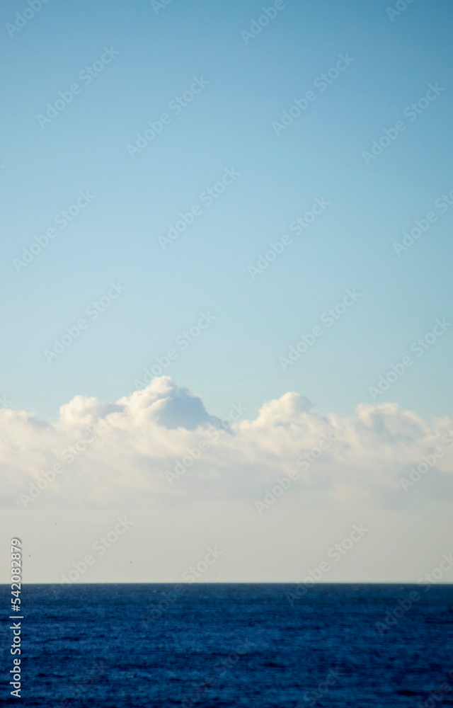 White cumulus clouds over the blue surface of the sea on sunny day. Beautiful natural background. Movement of clouds in the sky. Sky landscape. Seascape. White blue colors. Place for text, copy space