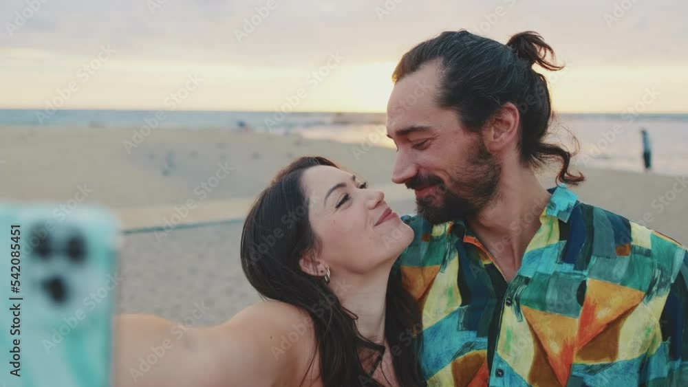 Loving couple laughing and kissing makes selfie on mobile phone while standing on the beach Loving couple laughing and kissing makes selfie on mobile phone while standing on the beach